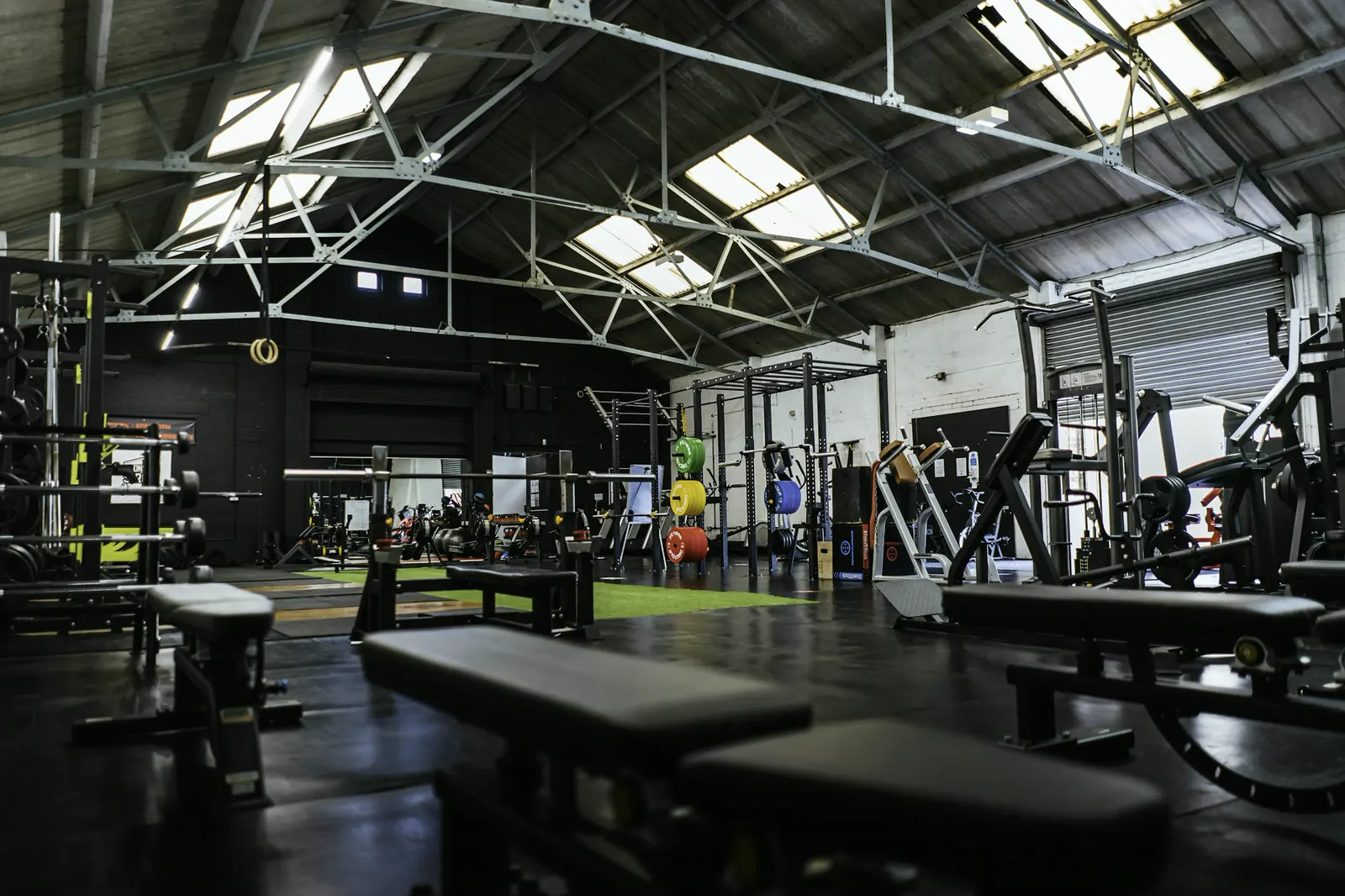 The main training floor at PACE The Domain: racks, benches and a turf lane under a high steel roof